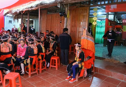 Cô dâu (trùm đầu) ngồi trước cửa nhà chú rể để thầy cúng thực hiện các nghi thức trong lễ cưới.