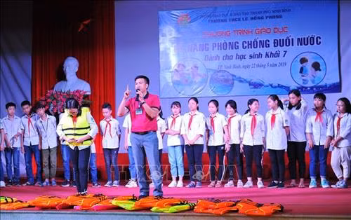 Cán bộ Trung tâm Thanh thiếu nhi tỉnh Ninh Bình hướng dẫn mặc áo phao đúng cách cho các em học sinh. Ảnh: Minh Đức - TTXVN