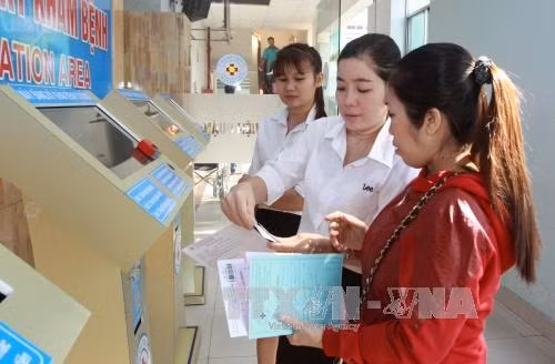 Nhân viên bệnh viện hướng dẫn bệnh nhân tại khu vực tự đăng ký và quẹt thẻ BHYT khám bệnh. Ảnh: Phương Vy-TTXVN