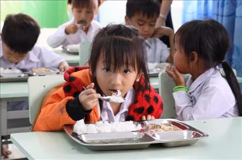 Các em học sinh tại trường Tiểu học và Trung học cơ sở Đinh Núp ăn bữa “Cơm có thịt Tây Nguyên” đầu tiên. Ảnh: Dư Toán – TTXVN.