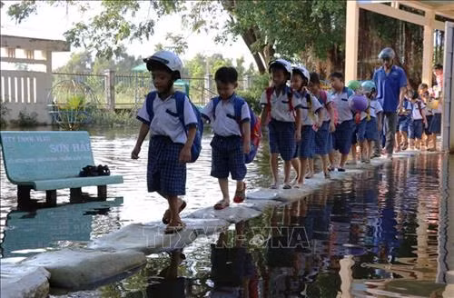 Sân trường Tiểu học Vĩnh Đại (Tân Hưng) ngập trong nước lũ, phụ huynh và giáo viên phải dùng bao cát đắp đường cho các em học sinh đi lại. Ảnh: Bùi Giang - TTXVN