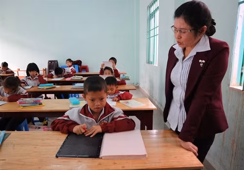 Một học sinh bị khiếm thị được cô giáo hướng dẫn làm bài tập tại lớp học Don Bosco