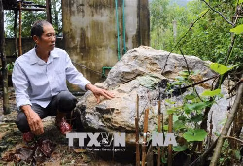 Ông Quàng Văn Sơn, người dân bản Pa Xa Xá, bên tảng đá gần 4m3 rơi từ trên núi, lăn qua nhiều hộ dân khác trước khi rơi xuống cạnh khu vực nhà bếp của gia đình ông vào năm 2017. Ảnh: Xuân Tiến