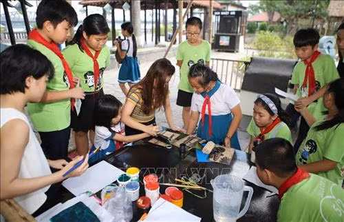 Các em học sinh thích thú với trải nghiệm làm tranh tại không gian triển lãm. Ảnh: Hồ Cầu-TTXVN