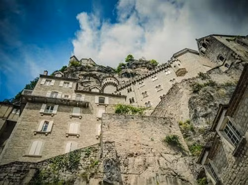 Ngôi làng cổ Rocamadour được xây dựng trên vách núi ở vùng Occitanie, miền tây nam Pháp. Từ thời Trung cổ, ngôi làng đã thu hút những người hành hương từ khắp châu Âu tới đây tham quan các công trình lịch sử và nhà thờ Đức Mẹ Maria. Thánh St Amator đã sống và qua đời tại ngôi làng Rocamadour ngay sau khi ông rời khỏi Jerusalem. Truyền thuyết kể rằng sau khi thi thể thánh St Amator được phát hiện, một số phép màu đã xảy ra. Ngôi làng bắt đầu thu hút nhiều người hành hương và ủng hộ từ các nhà vua Pháp, giúp ngôi làng xây dựng các nơi thờ cúng. Một lý do khác khiến Rocamadour thu hút nhiều du khách là phong cảnh đẹp. Các công trình cổ được xây dựng trên vách núi nhìn xuống sông Alzou. Các tòa nhà trong làng có độ cao cách mặt đất phía dưới khoảng 120m. Trung tâm của ngôi làng là nhà thờ hành hương Notre Dame, được cải tạo lại từ công trình gốc được xây dựng từ năm 1479. Ngoài ra, Rocamadour còn có nhiều công trình cổ kính khác được xây dựng từ thời Trung cổ. Du khách tham quan dọc một con đường dốc tại ngôi làng cổ Rocamadour. Những ngôi nhà được xây dựng trên vách đá dựng đứng.