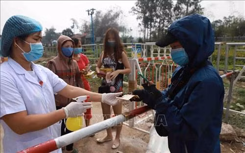 Nhân viên y tế chốt kiểm soát số 1 xã Sơn Lôi xịt khử khuẩn tiền trước khi thanh toán giao nhận hàng qua chốt kiểm soát số 1 tại xã Sơn Lôi. Ảnh: Hoàng Hùng - TTXVN
