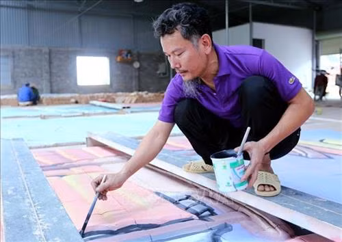 Nghệ nhân Lưu Xuân Khuyến đang hoàn thiện bức tranh gốm. Ảnh: Danh Lam - TTXVN