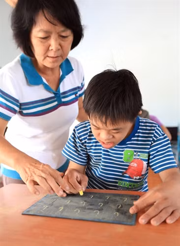 Các cô trong Trung tâm đang hướng dẫn các em viết chữ,
