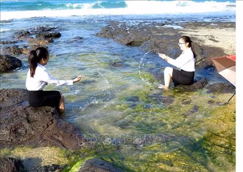 Du khách thích thú vui đùa cùng sóng biển bên bãi đá rêu xanh. Ảnh: Phước Ngọc-TTXVN