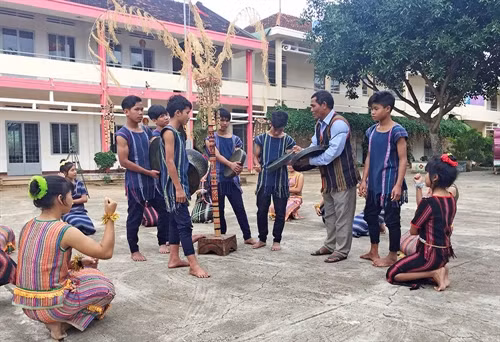 Già làng K’Bon hướng dẫn nhóm học sinh tập lại bài chiêng ngay giữa sân Trường Dân tộc nội trú Di Linh. Ảnh: N. Dũng