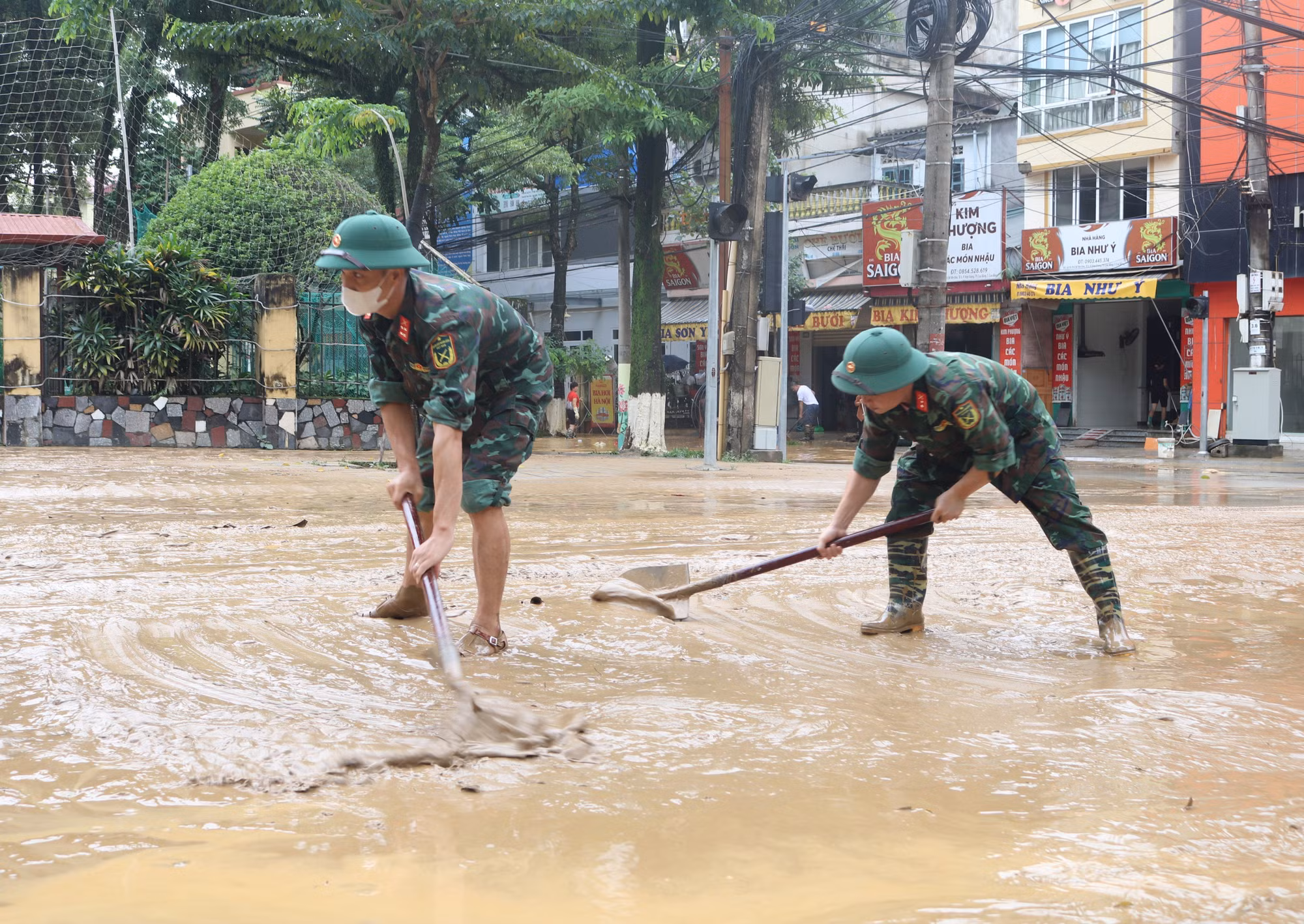 Lực lượng chức năng dọn dẹp bùn đất những đoạn đường phố nước đã rút. Ảnh: Chu Hiệu/TTXVN