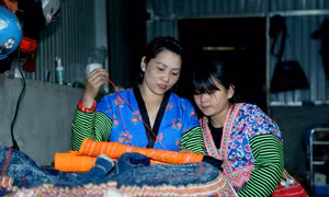 Chị Lầu Thị Tro hướng dẫn con gái cách thêu hoa văn trên trang phục truyền thống. Ảnh: Quang Quyết