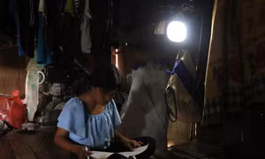 Em Đinh Thị Khơ, làng Mang Ve, học bài dưới ánh đèn năng lượng nguồn sáng yếu ớt. Ảnh: Phạm Cường-TTXVN T 