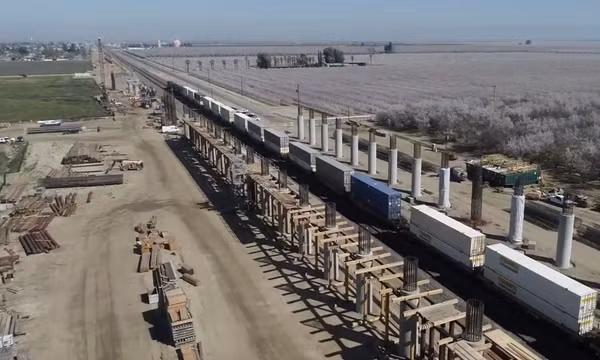 Ảnh chụp màn hình từ video quay bằng thiết bị bay không người lái vào tháng 3/2020 ghi lại quá trình xây dựng cầu cạn Wasco, một phần của dự án đường sắt cao tốc California. Có thể thấy một đoàn tàu BNSF đang đi qua các cột đỡ đang được dựng lên ở hai bên đường ray chở hàng. Tuyến đường sắt cao tốc tương lai sẽ băng qua các đường ray này trên cầu cạn. Ảnh: Wikimedia Commons