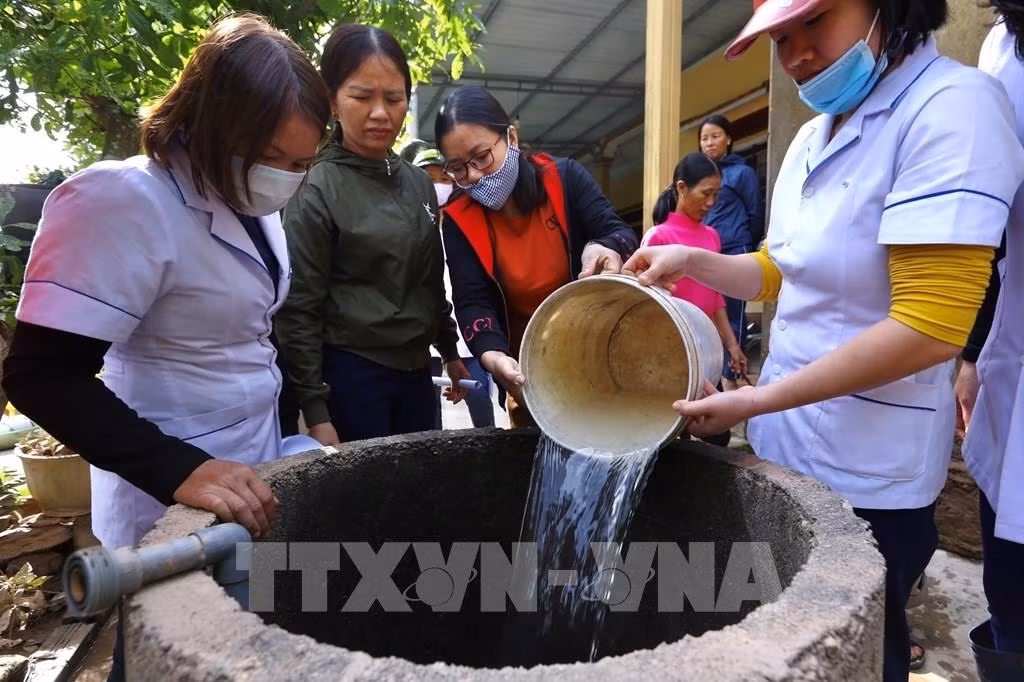 Nhân viên y tế tiến hành pha dung dịch hóa chất rồi đổ xuống giếng theo đúng quy trình và tỷ lệ cho phép để xử lý nguồn nước sinh hoạt an toàn cho người dân . Ảnh: Minh Quyết - TTXVN