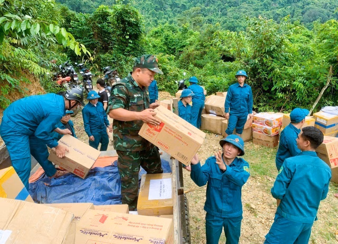 Các lực lượng tham gia bốc dỡ hàng hóa, nhu yếu phẩm, lương thực từ xe đầu kéo xuống điểm tập kết bên đường độc đạo giữa đại ngàn Pù Huống để dùng xe máy chờ vào cho bản làng Na Ngân. Ảnh: TTXVN phát