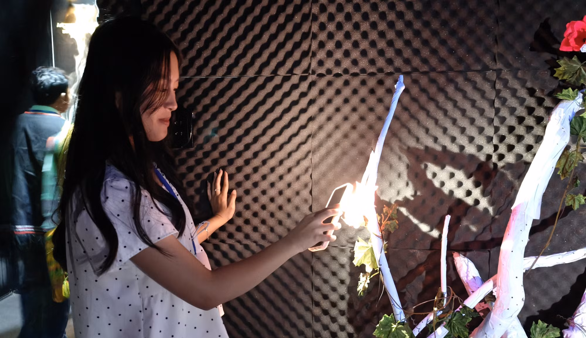 Du khách sử dụng ánh sáng từ điện thoại chiếu vào các bông hoa trong không gian “Âm thanh của gỗ” tại Nhà triển lãm Âm thanh, tạo nên những thanh âm và giai điệu khác nhau thông qua hệ thống cảm biến tương tác.
