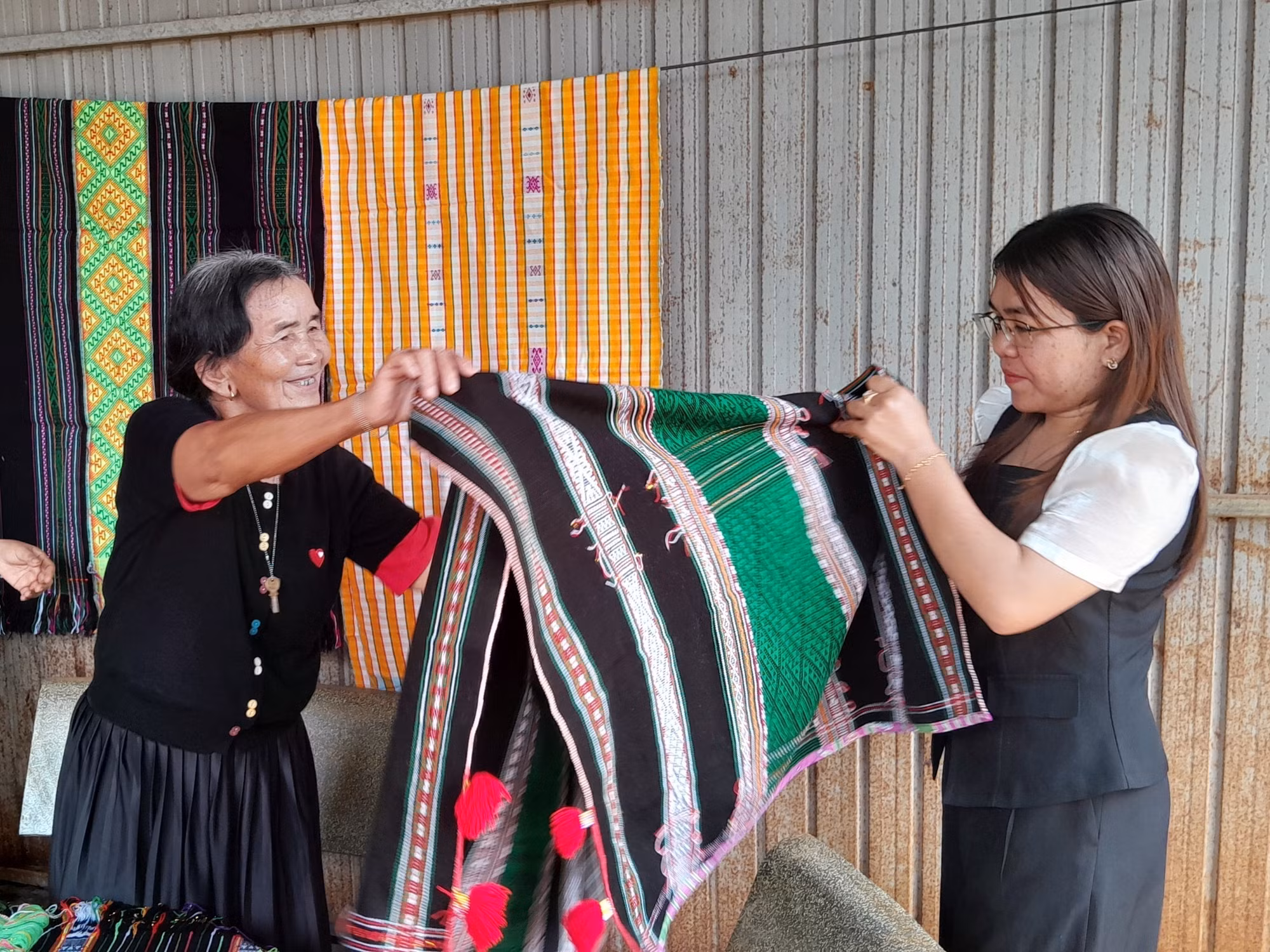 Bà Thị Y Rơ (76 tuổi, người dân tộc M’nông) giới thiệu tấm thổ cẩm đã hoàn chỉnh cho chuyên viên phòng văn hóa-xã hội xã Bù Gia Mập.
