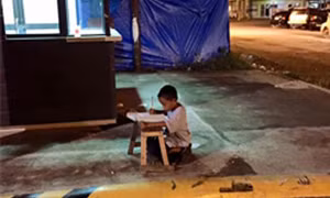 Xúc động cậu bé vô gia cư học bài dưới ánh đèn hắt từ nhà hàng