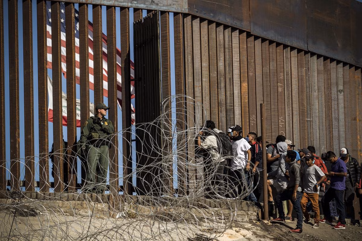 Người nhập cư trái phép đứng chờ ở hàng rào biên giới Mỹ-Mexico.